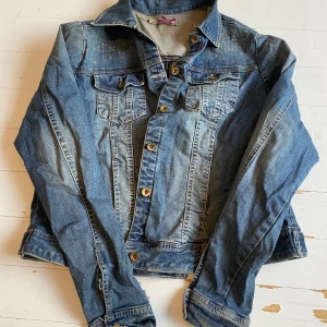Blå jeansjacka från Havanna - Säljer en klassisk blå jeansjacka från Havanna med knappar framtill och två bröstfickor. Jackan har en avslappnad stil med slitna detaljer som ger den en vintagekänsla. Perfekt för en casual look! Är lappad på höger arm(bild 5) och har lim räster från gammla patches på ryggen samt i fram. Pris kan diskuteras vid snabba affär!!