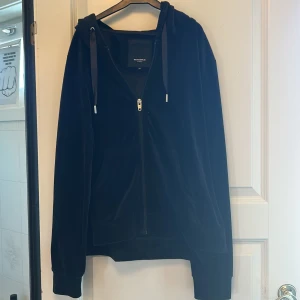 Svart hoodie från Rockandblue - Säljer en svart hoodie från Rockandblue med dragkedja och huva. Tröjan har ett snyggt tryck på ryggen med texten 'ROCKANDBLUE SWEDEN' och stjärnor. Perfekt för en avslappnad stil.