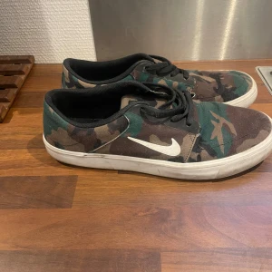 Camouflage sneakers från Nike - Snygga sneakers från Nike med ett coolt camouflage-mönster. Skorna har en vit sula och klassisk snörning. Perfekta för en avslappnad stil.