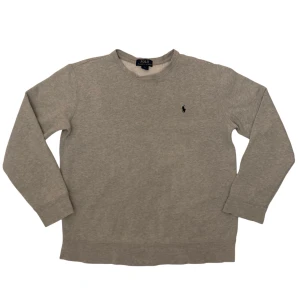 Grå Ralph Lauren Tröja - Säljer en stilren grå tröja från Polo Ralph Lauren med det klassiska broderade logotypen på bröstet. Tröjan har långa ärmar och en rund halsringning, perfekt för en avslappnad look. Tröjan är i storleken 14-16. Kom gärna med prisförslag eller frågor😇