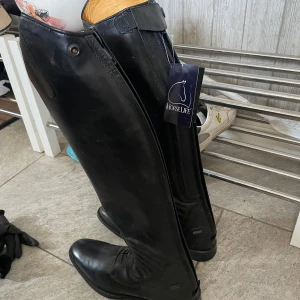 Svarta ridstövlar från Horse Life - Säljer ett par eleganta svarta ridstövlar från Horse Life. De är höga med snörning och dragkedja för enkel på- och avtagning. Nya med lapp kvar. Normal i bredd och längd på skaft. 