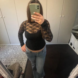  fest tröja - Snygg svart spetsblus med långärmad design och öppen rygg. Perfekt för en stilfull look. Blusen har ett vackert spetsmönster som ger en elegant touch.