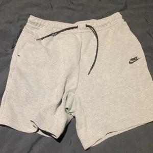 Grå och svarta shorts från Nike - Säljer två par bekväma shorts från Nike. Ett par är ljusgrått och det andra är svart, båda med dragsko i midjan och Nike-logga på sidan. Perfekta för en avslappnad stil eller träning.