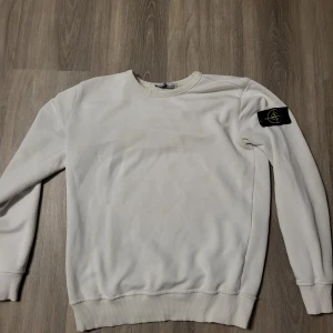 Vit tröja från Stone Island - Säljer en stilren vit tröja från Stone Island med deras ikoniska märke på ärmen. Tröjan har långa ärmar och ribbade muddar vid ärmslut och nederkant. Perfekt för en casual look. Och priset kan diskuteras