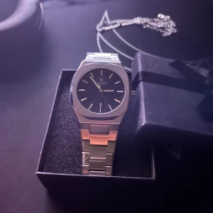 Silver klocka med svart urtavla - Elegant klocka från Tayroc med en stilren svart urtavla och silverfärgad metallarmband. Perfekt för den som söker en tidlös accessoar med modern touch.