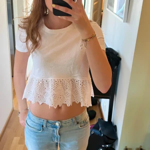 Vit kortärmad topp med spetsdetaljer - Säljer en söt vit topp med korta ärmar och en fin spetsvolang nedtill. Perfekt för sommardagar och ger en romantisk touch till din outfit. Toppen är croppad och har en normal passform.