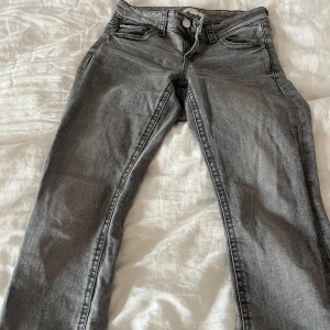 Grå jeans från Gina Tricot - Snygga grå lågmidjade jeans från Gina Tricot i storlek 158. De har en klassisk femficksdesign med dragkedja och knapp framtill. Perfekta för en avslappnad stil.