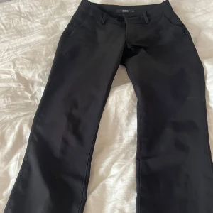 Svarta kostymbyxor från Bik Bok - Snygga lågmidjade svarta kostymbyxor från Bik Bok med en klassisk design med slits nere. Byxorna har en rak passform och är perfekta för en stilren look. De har hällor för bälte och en diskret dragkedja framtill.