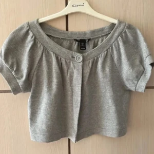 Grå kortärmad kofta/bolero - Säljer en söt grå kortärmad kofta/bolero från H&M❤️‍🔥 Den har en knapp framtill och en rund halsringning. Perfekt för lager-på-lager-stil eller som ett lättare plagg under varmare dagar🙏🏼