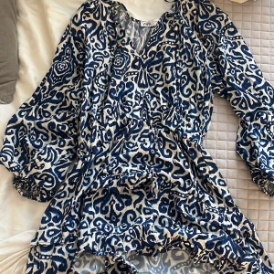 Mönstrad klänning från Zara - Säljer en snygg mönstrad klänning från Zara i blått och vitt. Klänningen har långa ärmar och en v-ringad design med volangdetaljer. Perfekt för en stilfull look! Säljer pga att den är lite kort på mig för min smak, jag är 166❣️pris kan diskuteras!