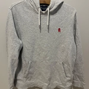 Grå bondelid hoodie - Säljer en stilren grå hoodie med en liten röd broderad logga på bröstet. Tröjan är i strl L och har inga defekter