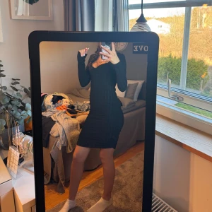 Svart klänning med lång ärm - Snygg svart klänning med lång ärm och figurnära passform. Perfekt för en stilren look. Klänningen har en enkel design som framhäver silhuetten.