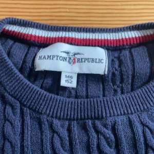 Mörkblå kabelstickad tröja från Hampton Republic - Säljer en stilren mörkblå kabelstickad tröja från Hampton Republic. Tröjan har en broderad logga i rött på bröstet och ribbade muddar vid ärmslut och nederkant. Perfekt för kyligare dagar!