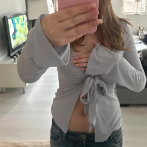 Grå knytblus med långa ärmar - Säljer en stilren ljusblå blus med knytning framtill. Blusen har långa ärmar med vida ärmslut och en v-ringad design. Perfekt för en trendig look .intemisimi liknande 💓
