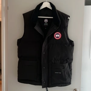 Freestyle Crew Vest  - Säljer en svart dunväst från Canada Goose med deras ikoniska märke på bröstet. Västen har knappar och dragkedja framtill samt praktiska fickor. Perfekt för kyliga dagar. För ytterligare information skriv gärna till mig. 