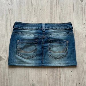 Blå lågmidjad jeanskjol  - Ljusblå lågmidjad jeanskjol från Tom Tailor som jag har sytt upp från en längre kjol. Storlek 36. Tvärs över midjan är det 38 cm+ lite stretch och den är 29 cm lång. Fint skick. Använd gärna köp nu!