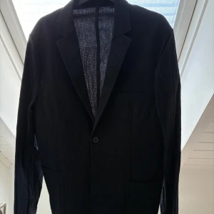 Svart kavaj från H&M - Snygg svart kavaj från H&M i storlek M. Kavajen har en klassisk design med knapp framtill och två fickor. Perfekt för en stilren look. Tunnare material passar perfekt till varmare väder. 
