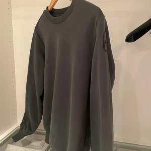 Mörkgrön tröja från Parajumpers - Säljer en stilren mörkgrön tröja från Parajumpers med ett märke på ärmen. Tröjan har långa ärmar och en ribbad krage samt muddar vid ärmslut och nederkant. Perfekt för en avslappnad look. Skick 8/10 använd ett par gånger.