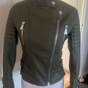Olivgrön skinnjacka med dragkedjor - Snygg olivgrön skinnjacka med asymmetrisk dragkedja. Jackan har flera dragkedjor och spännen i midjan för en justerbar passform. Säljer pga att den tyvärr inte sitter bra på mig, lite avskad på insidan men inget som syns när man har på sig den 💚pris kan diskuteras