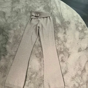 Beige stickad hoodie och byxor - Säljer ett set med en beige stickad hoodie och matchande byxor. Hoodien har dragkedja och snörning i huvan, medan byxorna har en ribbad midja med dekorativt bälte. Perfekt för en avslappnad stil.