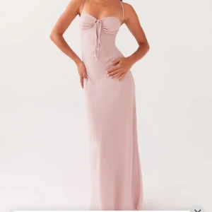 Balklänning - Elegant ljusrosa långklänning med smala axelband och vacker snörning i ryggen. Klänningen har en knytning framtill och en figurnära passform som ger en stilren look.