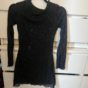 Svart glittrig klänning - Snygg svart klänning med glittrande detaljer och långärmad design. Den har en åtsittande passform och en elegant öppen rygg. Perfekt för en kväll ute!