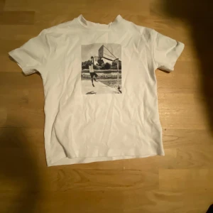 Vit t-shirt med tryck - Säljer en vit t-shirt från D.M.D med ett coolt svartvitt tryck på framsidan. T-shirten har korta ärmar och är perfekt för en avslappnad stil. Passar bra till jeans eller shorts för en casual look.