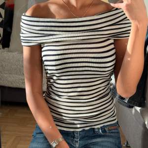 Snygg randig offshoulder topp i svart och vit. Den har en ribbad struktur och en tight passform som framhäver figuren. Perfekt för en stilren och trendig look.