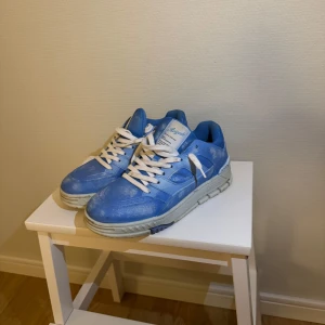 Blå sneakers från Axel Arigato - Snygga limiterade ljusblå sneakers med moln liknande märken från Axel Arigato med vit sula och vita snören. Skorna har en modern design med en rund tå och är perfekta för en stilren look. De är tillverkade i ett syntetmaterial som ger en skön passform. Ny pris 3000. Väldigt bra skick. Passar 39-40