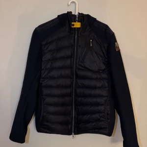 Marinblå cardigan från Parajumpers - Säljer en cardigan från Parajumpers med dragkedja och luva. Jackan har en quiltad design och en praktisk bröstficka med dragkedja. Enbart 1 ägare som knappt använt så skickat är nyskick. Hör av er vid frågor