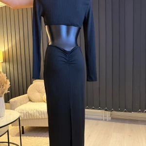 Svart ribbad långklänning - Elegant svart långklänning med ribbad textur och långärmad design. Klänningen har en smickrande passform med en subtil rynkning framtill och en slits för extra stil. Perfekt för en chic och sofistikerad look. Passar perfekt som oversize modell (s/m/l storlek). Jag rekommenderar den varmt. 👌🌸