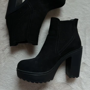 Svarta mocka boots med klack - Snygga svarta boots i mocka med hög klack och rund tå. De har elastiska sidor för enkel på- och avtagning. Perfekta för att ge lite extra höjd och stil till din outfit! Märke XIT, storlek 38. Oanvända pga fel storlek. Frakt tillkommer om du önskar att få skorna hemskickade istället för att hämta i Umeå!