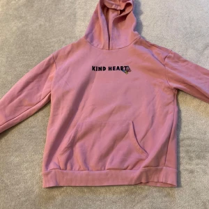 Rosa hoodie med fjärilstryck - Säljer en rosa hoodie med texten 'Kind Heart' på framsidan och ett stort fjärilstryck på baksidan. Hoodien har en klassisk känguruficka och ribbade muddar vid ärmslut och nederkant. Perfekt för en avslappnad stil!