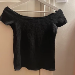 Svart offshoulder topp - Snygg svart offshoulder topp med korta ärmar. Bara använd några gånger normal i storleken. Inte helt slätt tyg utan något mönsterliknande men jättefin på🤩