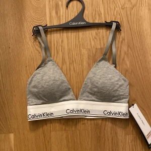 Grå triangeltopp från Calvin Klein - Säljer en grå triangeltopp från Calvin Klein med justerbara axelband och elastiskt band med logga under bysten. Toppen är lätt vadderad och har en bekväm passform.