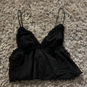 Svart topp - Säljer en elegant svart linnetopp med tunna axelband och spetsdetaljer. Toppen har en v-ringad design och är perfekt för en stilren look. Materialet är mjukt och bekvämt.