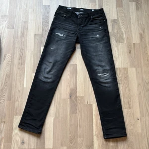 Svarta Jack & Jones jeans med slitningar - Säljer ett par riktigt feta slim fit jeans ifrån Jack and Jones med coola slitningar på framsidan. Perfekta för en trendig look. De är i storlek 158/13Y men jag är 172 cm och de passar mig vädigt bra. Om man gillar att ha lite mer slim fit. De här säljs inte mer.                                                 Ny pris ca 500kr men hos oss 249kr!                  Vid frågor eller funderingar är det bara att höra av sig!✌️💯🙌