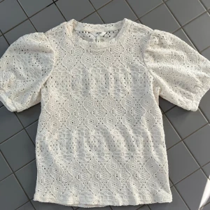 Vit blus från Object - Säljer en söt vit blus från Object med puffiga kortärmar. Blusen har ett fint mönster med som små hål och rund halsringning. Perfekt för en sommaren! Den är i bra skick och nästan inte använd, kom gärna privat för frågor eller fler bilder ☺️