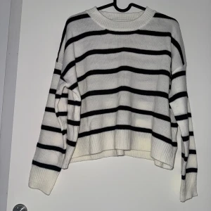 Vit och svart randig tröja - Aldrig använd! Säljer en snygg vit och svart randig tröja med långa ärmar. Tröjan är gjord av 100% akryl och har en bekväm passform. Perfekt för en stilren look.