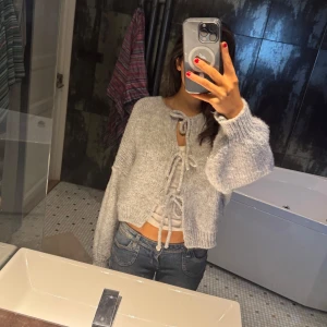 Grå stickad kofta med knytning -  grå stickad kofta med knytning framtill. Koftan har långa ärmar och en croppad passform, passar både Medium och Small, använd 1 gång!💕