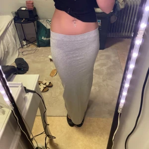 Grå långkjol - Säljer en stilren grå långkjol som är perfekt för en avslappnad look. Kjolen har en tight passform och är gjord i ett mjukt material som ger en bekväm känsla. Perfekt att matcha med en crop top eller en stickad tröja. Är 166 cm och passar mig bra 