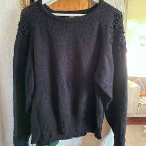 Svart tröja från BikBok - Säljer en svart tröja från BikBok med dekorativa pärlor på axlarna. Tröjan har en rund halsringning och långa ärmar. Fint skick men kommer tyvärr inte längre till användning!