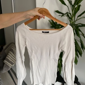 Vit ribbad topp från Gina Tricot - Säljer en stilren vit ribbad topp från Gina Tricot. Toppen har en elegant båtringning och långa ärmar, perfekt för en chic och enkel look. Passar bra till både jeans och kjol. Perfekt för alla säsonger!