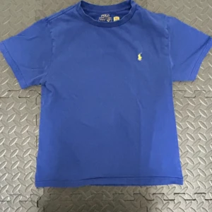 Blå t-shirt från Ralph Lauren - Snygg blå t-shirt från Ralph Lauren med det klassiska gula logotypbroderiet på bröstet. Perfekt för en avslappnad stil. Tillverkad i mjukt material för extra komfort.