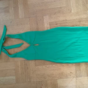 Grön klänning med knytband - Snygg grön klänning med knytband i nacken och en liten öppning framtill. Den sista bilden visar klänningens färg. Perfekt för en somrig look. Klänningen har en smickrande passform och är tillverkad i ett mjukt material.
