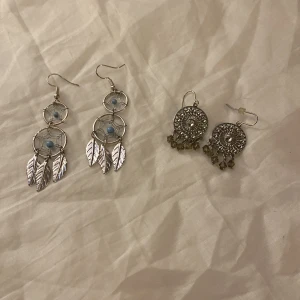 Två par örhängen med fjädrar och pärlor - Säljer två par unika örhängen. Ett par har silverfärgade fjädrar och blå pärlor i drömfångardesign. Det andra paret är silverfärgade med runda detaljer och hängande pärlor. Perfekta för att ge en bohemisk touch till din stil.