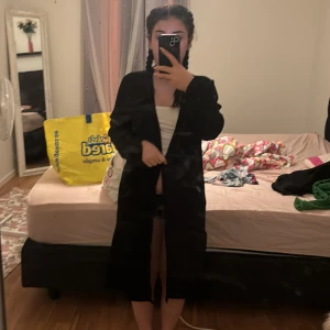 Svart lång kappa - Säljer en stilren svart lång kappa med normal passform. Perfekt för höst och vår, den har långa ärmar och en enkel design utan synliga detaljer. Ett mångsidigt plagg som funkar till många olika outfits.