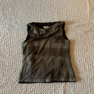 Glittrig ärmlös topp - Snygg glittrig topp i en mörk nyans. Den är ärmlös och har en stilren design som passar perfekt för en kväll ute. Toppen är tillverkad i ett glittrande material som ger en lyxig känsla.