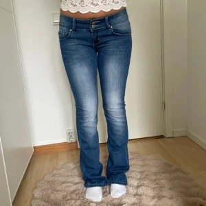 Blå bootcut jeans - Snygga blå bootcut jeans med en klassisk femficksdesign och knappgylf. Perfekta för en avslappnad stil med en touch av retro. De har en lätt tvättad look som ger en cool vibe.