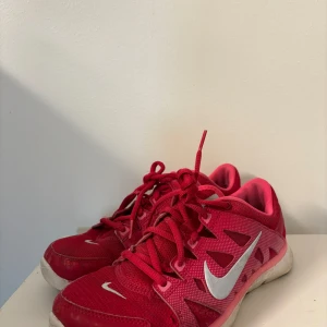 Röda Nike sneakers med snörning - Snygga röda Nike sneakers med vit swoosh-logga på sidan. Skorna har snörning och en sportig design, perfekt för träning eller vardagsbruk. De är tillverkade i syntetmaterial med en bekväm passform. Har jätte små hål på sidorna men inget som påverkar användningen eller syns så mycket. 